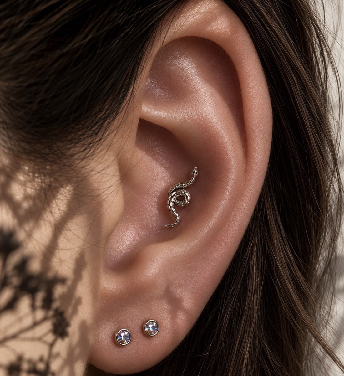 Silver-coloured serpent jewellery in a conch piercing, with two round gemstone lobe studs.