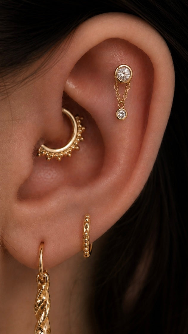 Curated ear with gold upper helix chain jewellery, beaded daith ring and chain drop lobe jewellery.