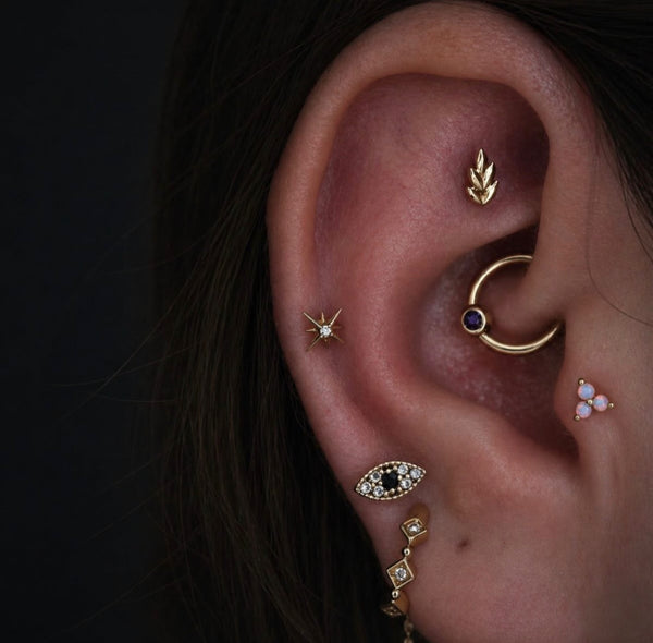 Curated ear styled with Junipurr Fernanda jewellery in a faux rook piercing, a Stella Star stud in the mid helix, an opal trinity stud in the tragus, a gold conch ring and diamond eye lobe jewellery for a luxury yellow gold ear stack.