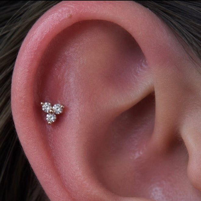 Close-up of a healed flat ear piercing featuring a Junipurr Trinity threadless end with three white cubic zirconia stones set in solid 14k gold, styled with a gold daith ring.