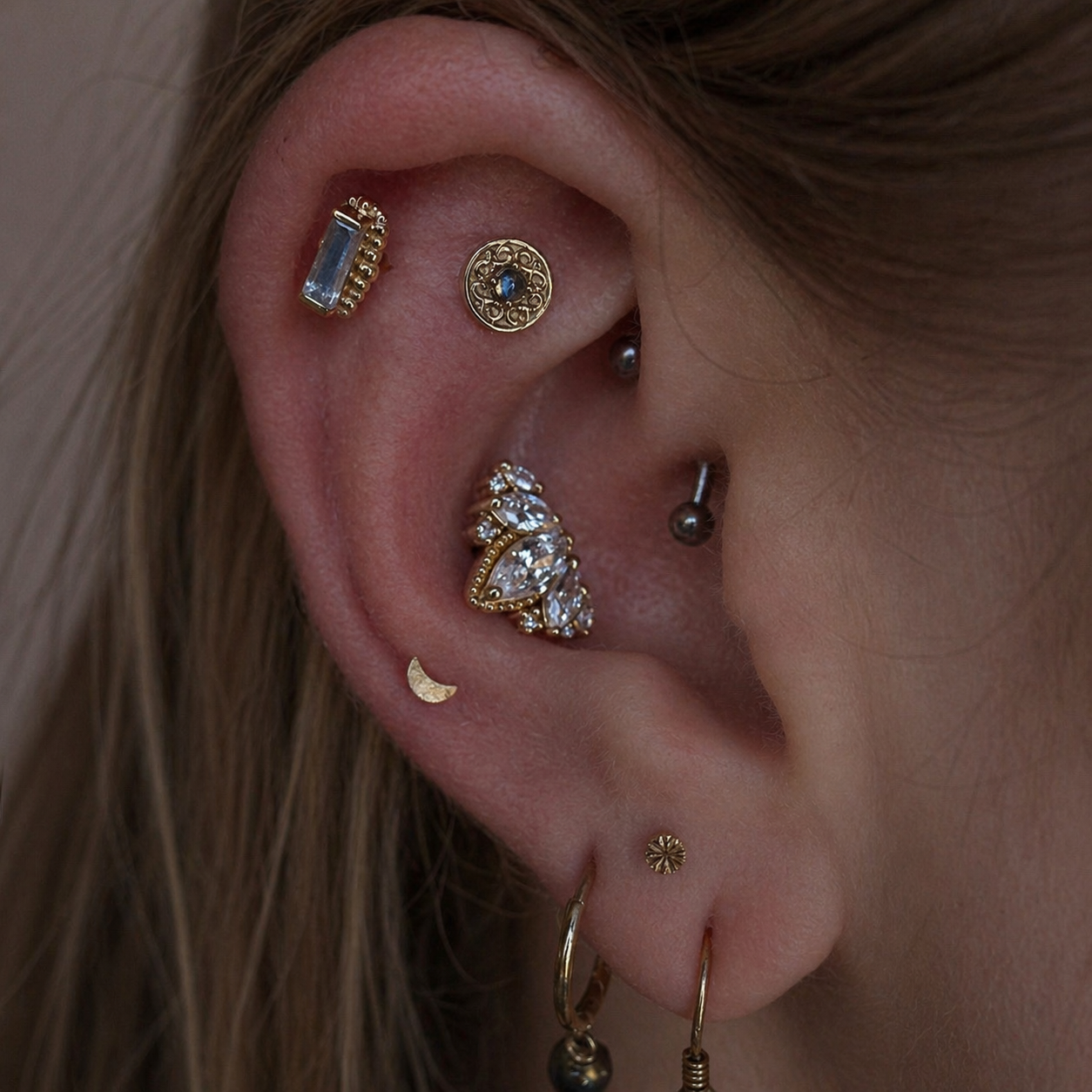 Curated ear featuring BVLA Elizabeth rainbow moonstone faux rook jewellery, BVLA beaded baguette rainbow moonstone flat helix end, Junipurr Queen Naveen conch jewellery, engraved Dusk stud and Love Moon stud in solid 14k gold.