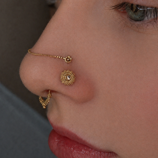 Close-up of luxury nose piercings featuring a BVLA Afghan 14k gold nostril stud, Junipurr box chain connecting a high nostril piercing, gold tri bead high nostril jewellery and a decorative gold septum ring in a curated facial piercing.
