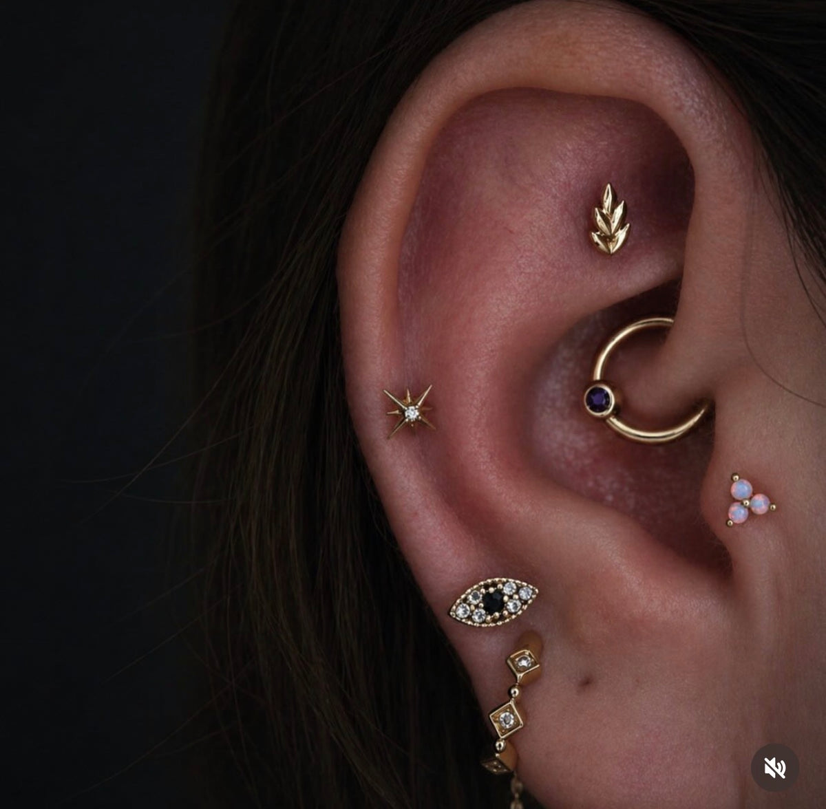 Close-up of a curated ear featuring a Junipurr Fernanda faux rook leaf, Stella mid helix star, white opal Trinity tragus stud, gold daith ring with purple gemstone, and luxury gold lobe jewellery.