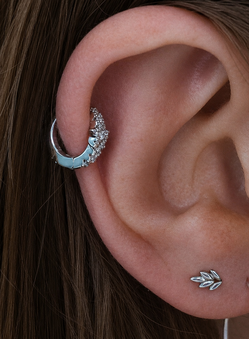 Close-up of a curated ear featuring a white gold Junipurr Fernanda helix ring with white gemstones and a white gold Fernanda leaf lobe stud in a minimalist luxury ear stack.