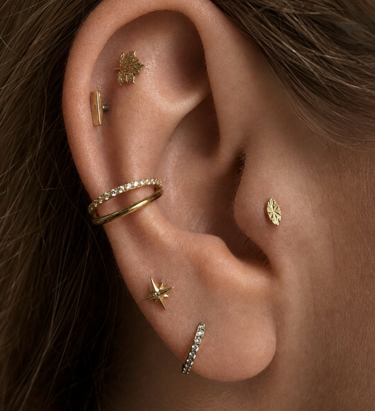 Curated ear with a Junipurr Laser Marquise stud, two conch hoops and other gold jewellery.
