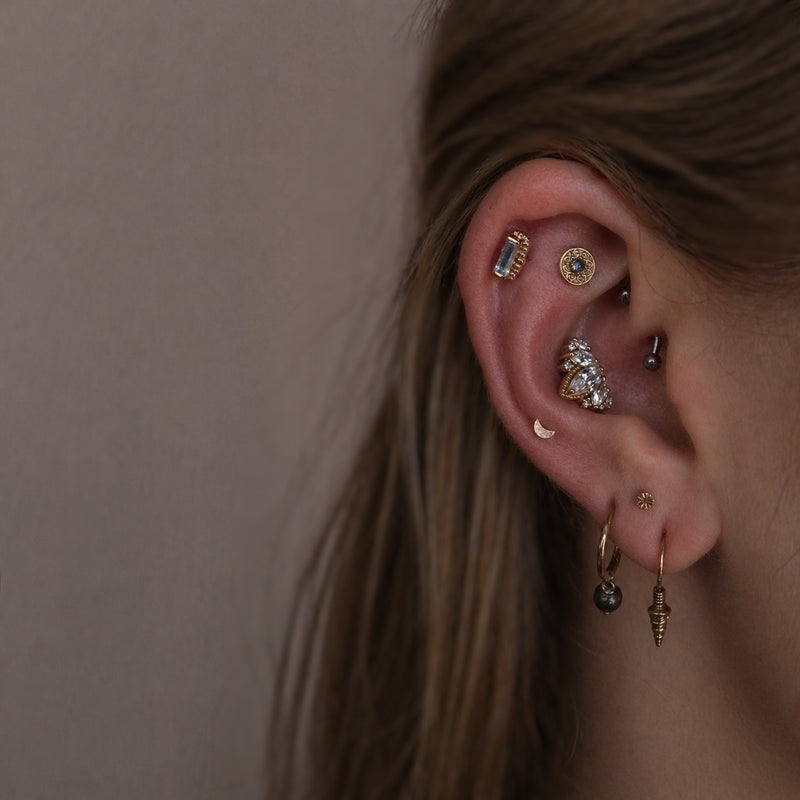 Luxury curated ear featuring the BVLA Rainbow Moonstone Beaded Baguette in the helix, Junipurr Elizabeth in the rook, Junipurr Queen Naveen in the conch, a moon mid helix stud and an engraved disc with stacked lobe jewellery.